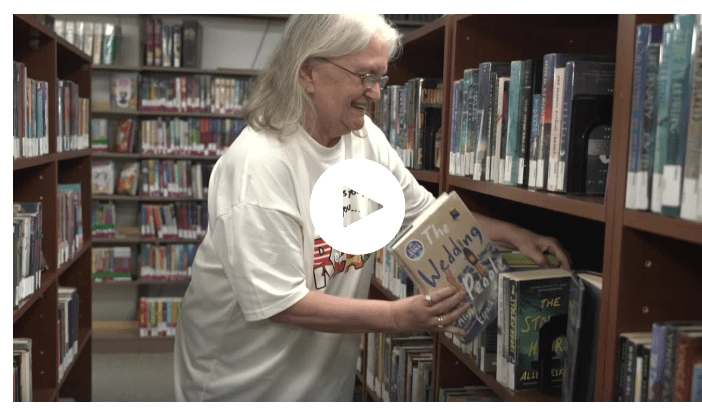 Person in a library placing a book titled "The Wedding" on a shelf.